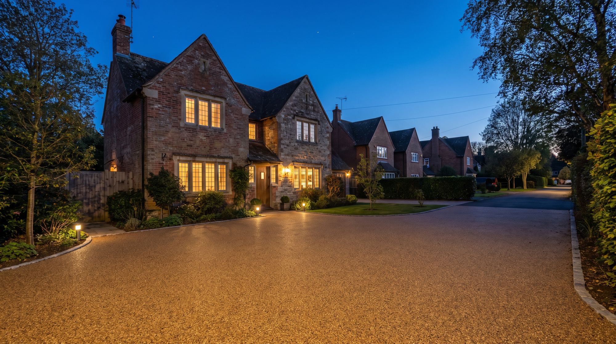 A resin bound driveway at dusk leading to a warmly lit English house